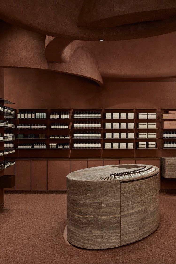 Бутик Aesop с терракотовыми стенами и овальной стойкой из травертина