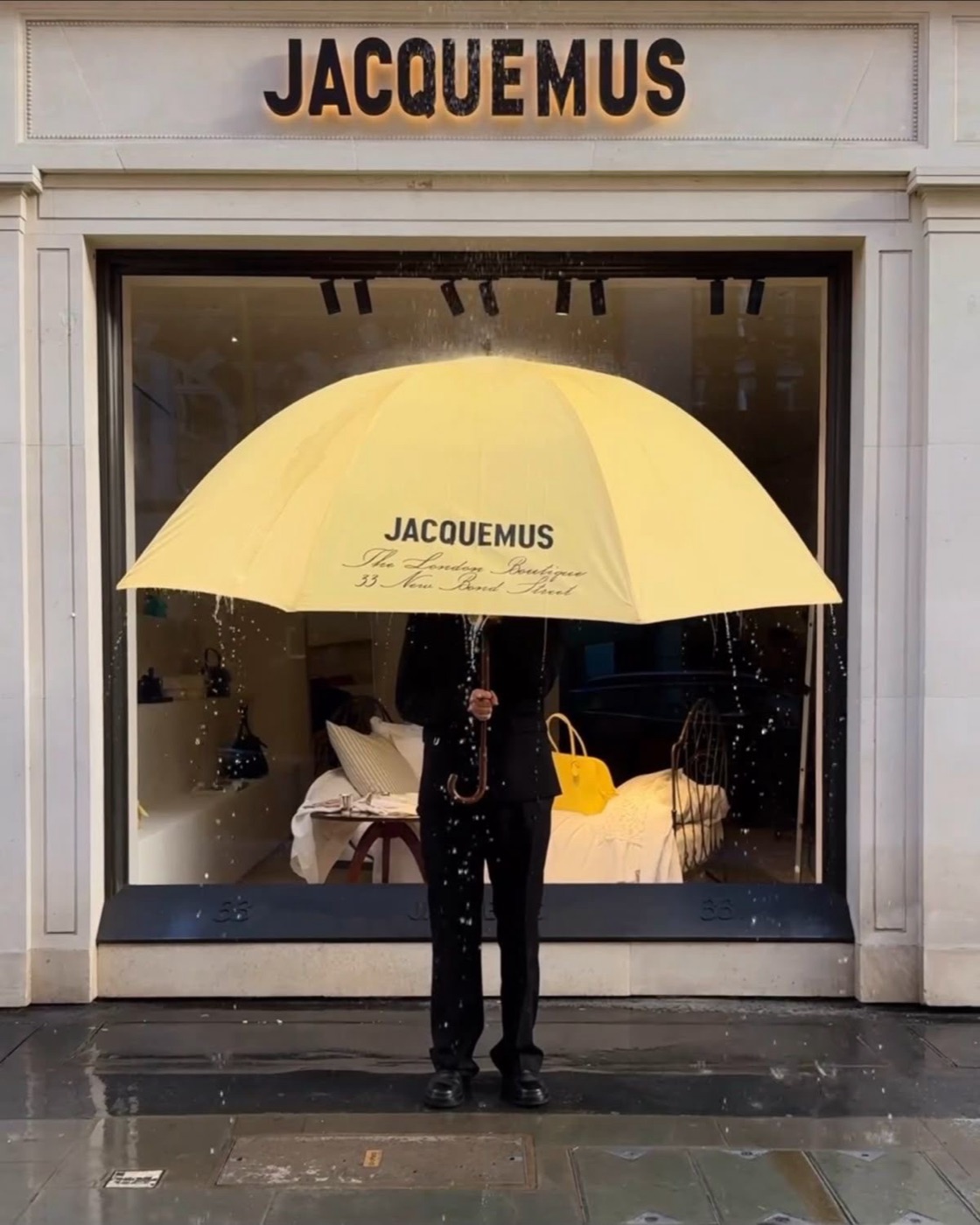 Человек под жёлтым зонтом Jacquemus у витрины лондонского бутика в дождь